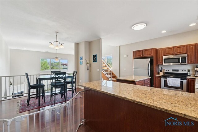 kitchen featuring dark wood-style flooring, recessed lighting, light stone counters, decorative light fixtures, and stainless steel appliances