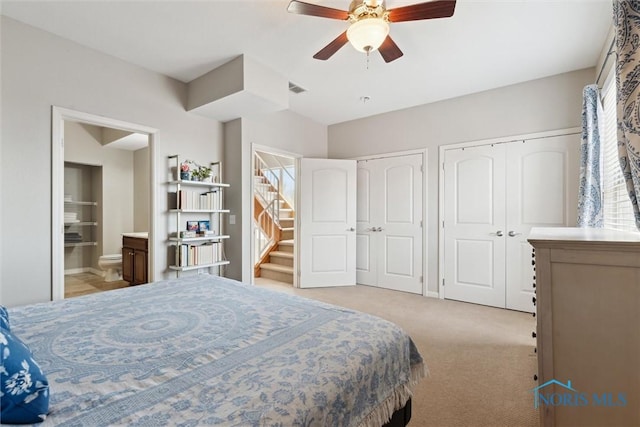 carpeted bedroom with a ceiling fan, two closets, ensuite bath, and visible vents