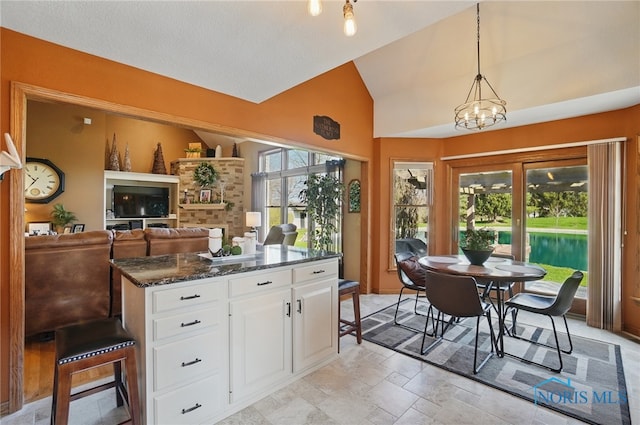 kitchen featuring a center island, dark stone counters, white cabinetry, lofted ceiling, and hanging light fixtures