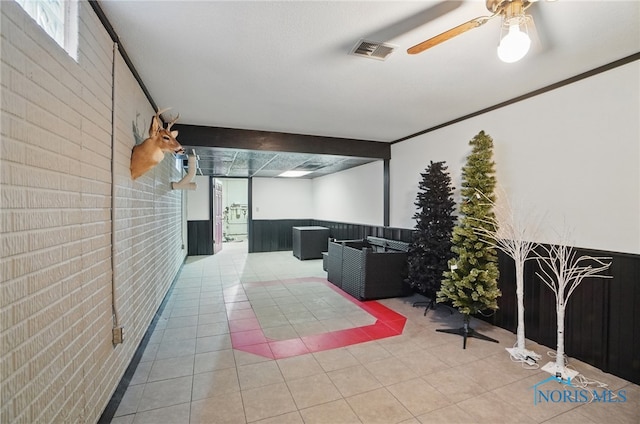 interior space featuring visible vents, a wainscoted wall, a ceiling fan, and brick wall
