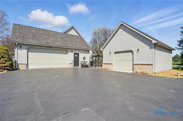 view of property exterior with a shingled roof, an outbuilding, brick siding, and a detached garage