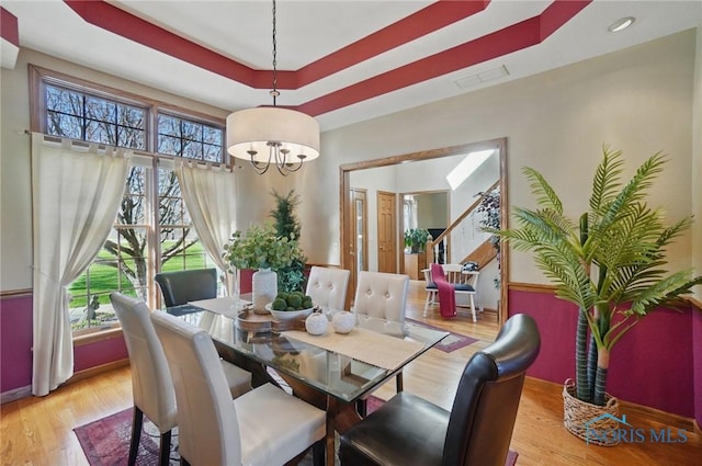 dining area with stairway, a chandelier, wood finished floors, and a raised ceiling