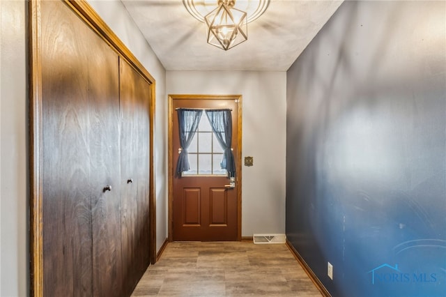 doorway to outside featuring baseboards, light wood finished floors, a chandelier, and visible vents