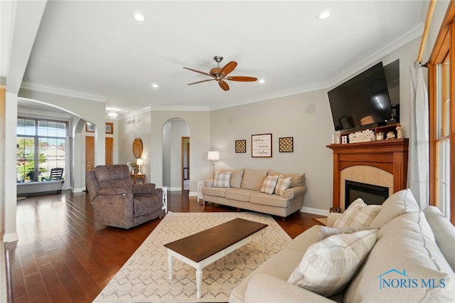 living area featuring ceiling fan, a tiled fireplace, arched walkways, recessed lighting, and dark wood-type flooring