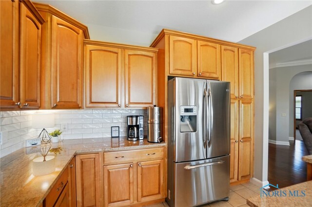kitchen featuring stainless steel fridge, arched walkways, backsplash, and light stone counters