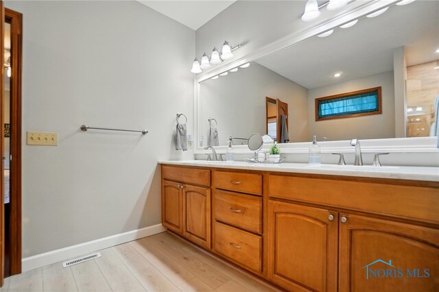 full bath featuring visible vents, double vanity, wood finished floors, baseboards, and a sink