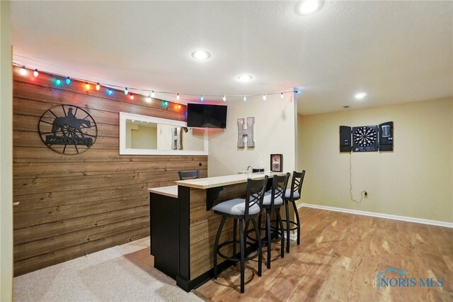bar featuring a bar, wood walls, baseboards, and recessed lighting