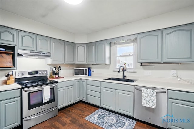 kitchen with under cabinet range hood, gray cabinets, appliances with stainless steel finishes, and a sink
