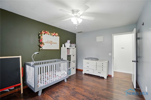 bedroom with visible vents, wood finished floors, baseboards, ceiling fan, and a nursery area