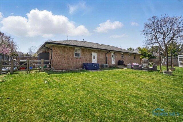 back of house with central AC unit, brick siding, a fenced backyard, an outdoor hangout area, and a yard