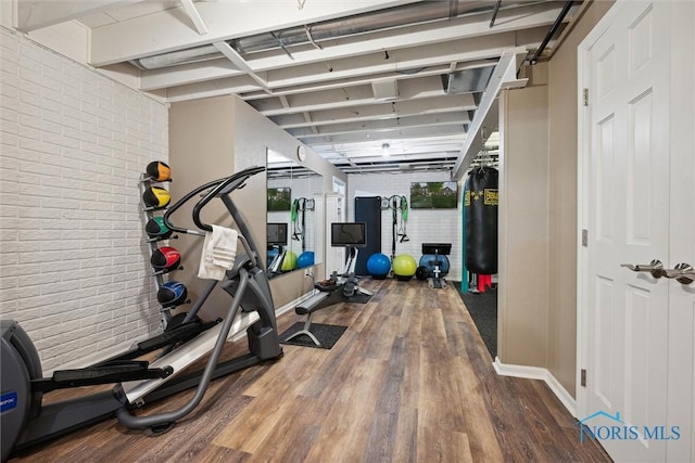 workout room with brick wall, baseboards, and wood finished floors