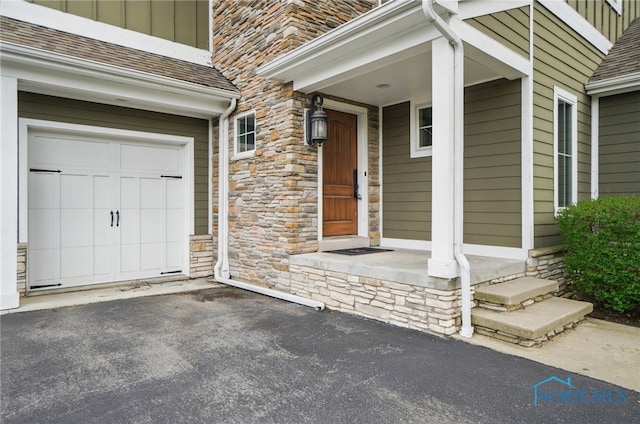 property entrance featuring a garage, board and batten siding, aphalt driveway, and stone siding