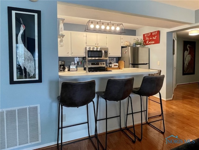 kitchen with white cabinets, stainless steel appliances, a peninsula, a kitchen breakfast bar, and visible vents