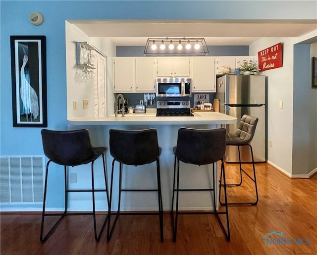 kitchen with a breakfast bar area, appliances with stainless steel finishes, light countertops, white cabinetry, and visible vents