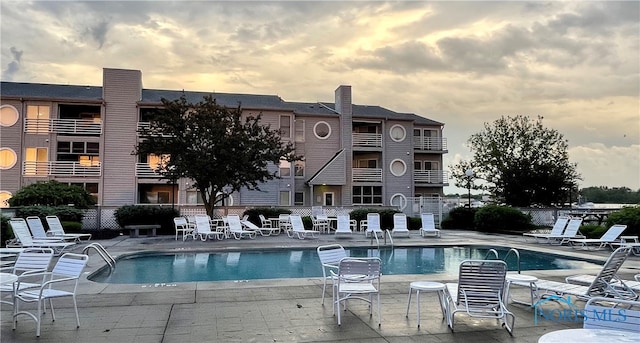 pool at dusk featuring a community pool, fence, and a patio