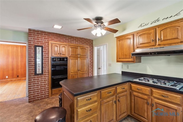 325 Park St, Bryan, OH 43506 - kitchen with under cabinet range hood, white gas cooktop, dark countertops, ceiling fan, and brown cabinetry