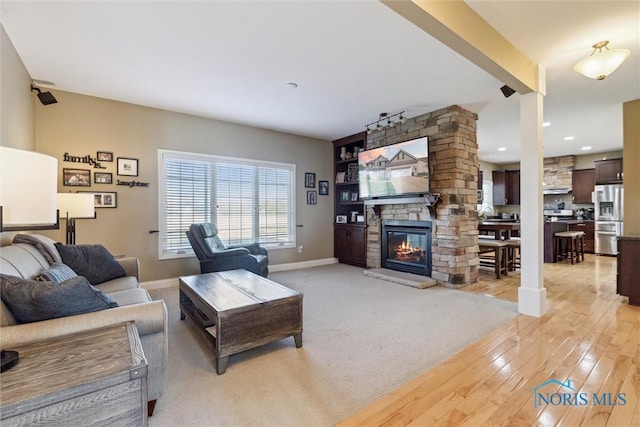 living area featuring recessed lighting, baseboards, light wood-type flooring, and a stone fireplace