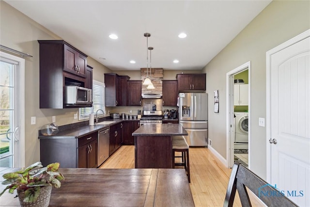 kitchen with a breakfast bar area, washer / clothes dryer, a sink, light wood finished floors, and stainless steel appliances