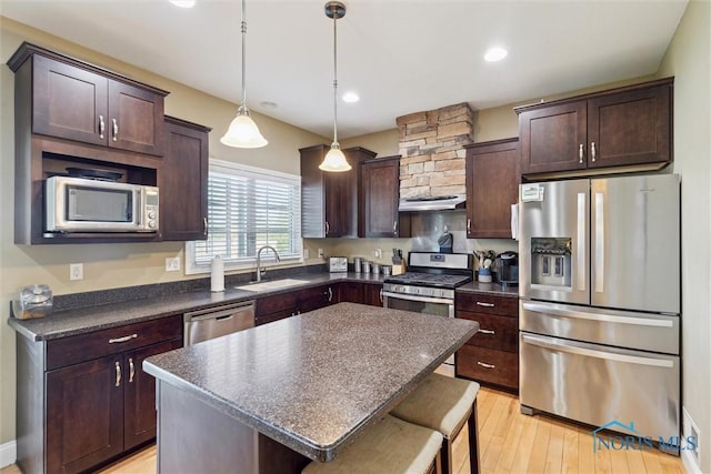 kitchen featuring a kitchen bar, dark countertops, dark brown cabinets, a sink, and stainless steel appliances