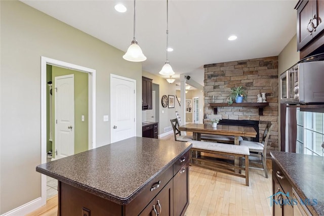 kitchen with pendant lighting, light wood-style flooring, dark brown cabinets, and dark countertops