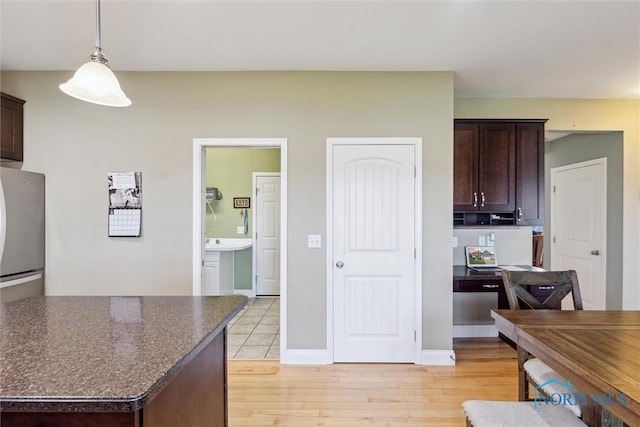 kitchen featuring decorative light fixtures, dark brown cabinets, baseboards, freestanding refrigerator, and light wood finished floors