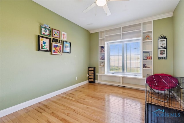 living area with ceiling fan, visible vents, built in shelves, wood finished floors, and baseboards