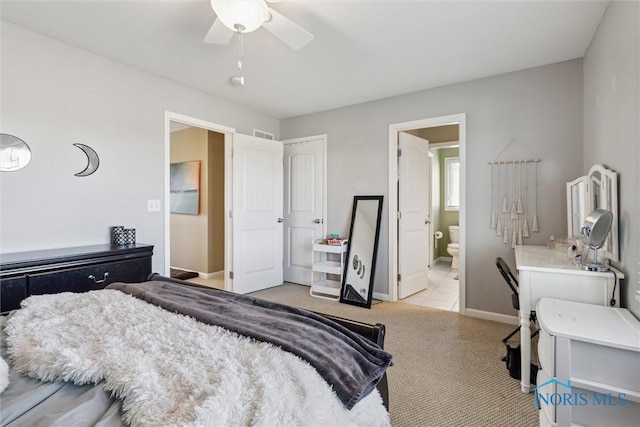 bedroom featuring ceiling fan, visible vents, light colored carpet, baseboards, and ensuite bath