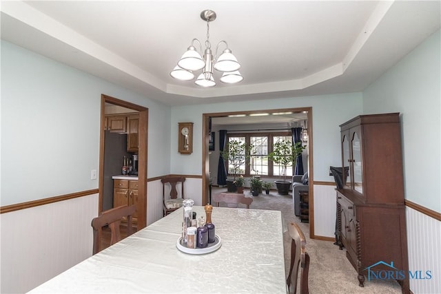 dining area with a raised ceiling, light carpet, a notable chandelier, and wainscoting