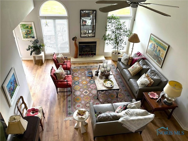 living room with a wealth of natural light, baseboards, wood finished floors, and ceiling fan