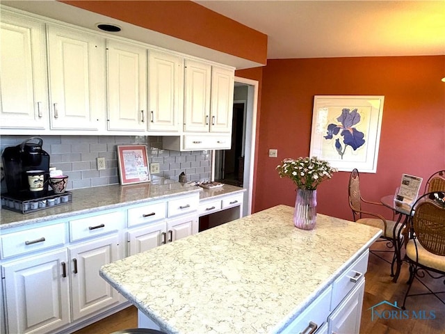 kitchen featuring dark wood-type flooring, a center island, tasteful backsplash, light stone counters, and white cabinets