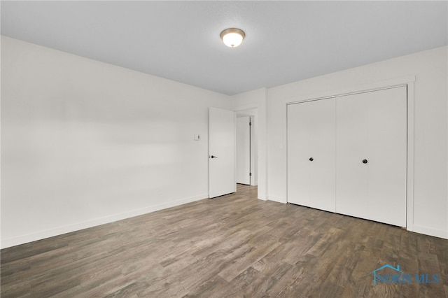 unfurnished bedroom with wood finished floors, a closet, and baseboards