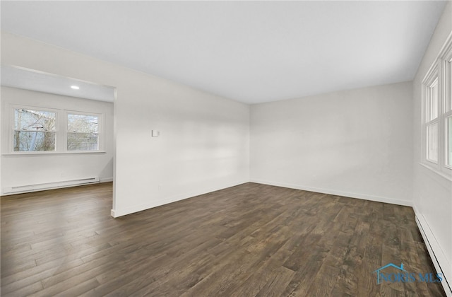 empty room with a baseboard heating unit, dark wood-type flooring, baseboard heating, and plenty of natural light