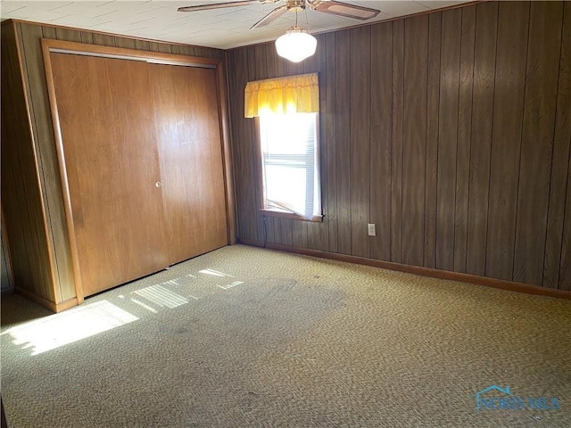 unfurnished bedroom featuring wooden walls, carpet floors, a closet, and ceiling fan