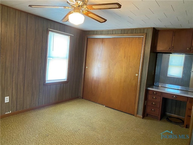 unfurnished bedroom featuring wooden walls, baseboards, a closet, and light colored carpet