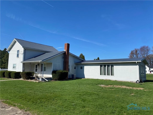 back of property featuring central AC unit, a lawn, a chimney, a porch, and metal roof