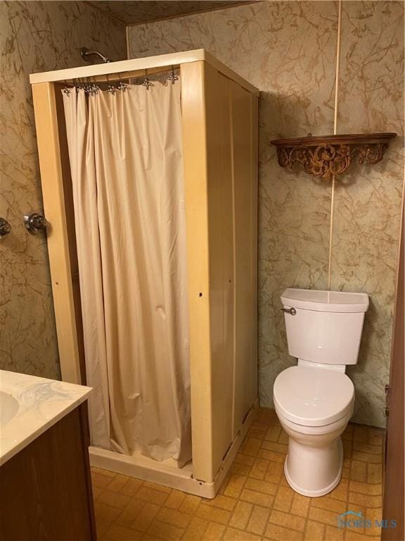 bathroom with toilet, vanity, wallpapered walls, and a stall shower