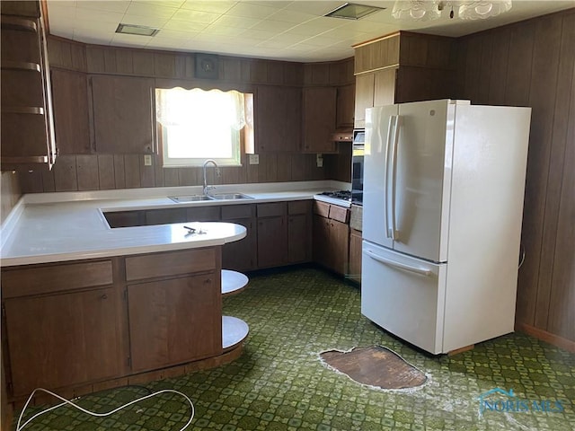 kitchen featuring a peninsula, a sink, wooden walls, freestanding refrigerator, and light countertops