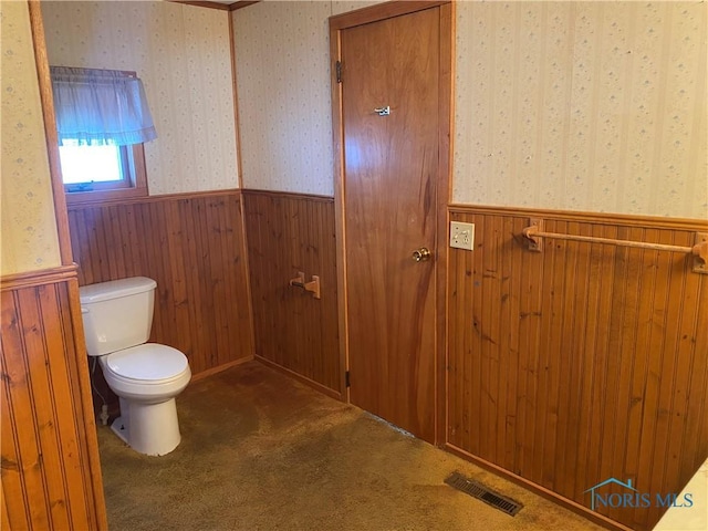 bathroom featuring wallpapered walls, wood walls, visible vents, toilet, and wainscoting