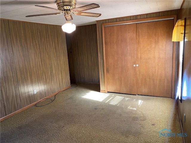unfurnished bedroom featuring a ceiling fan, carpet flooring, and wooden walls