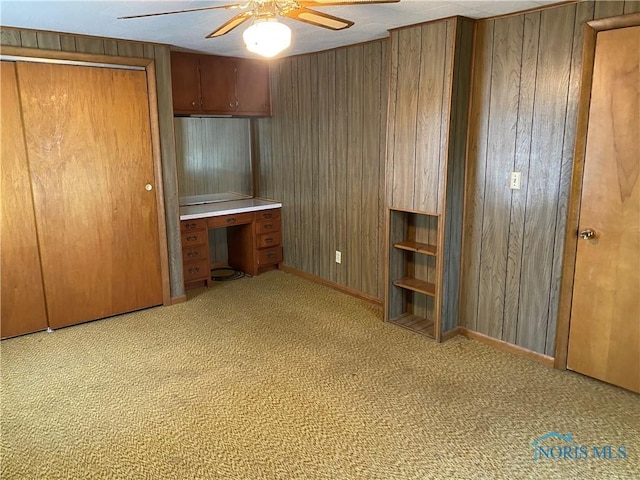 unfurnished bedroom featuring wooden walls, carpet flooring, baseboards, and a ceiling fan