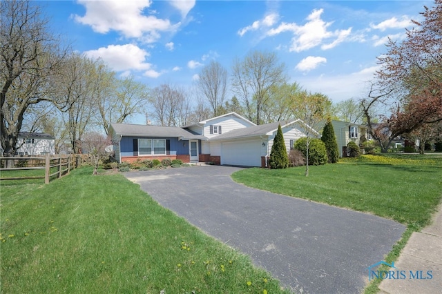 split level home featuring brick siding, fence, a garage, driveway, and a front yard