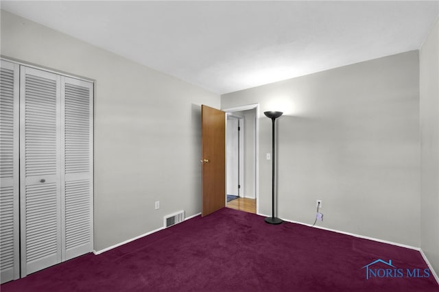 unfurnished bedroom featuring baseboards, visible vents, dark carpet, and a closet