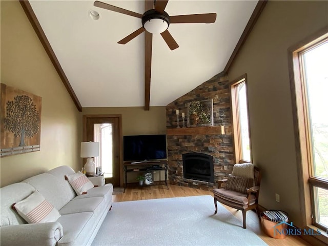 living area with wood finished floors, vaulted ceiling with beams, a stone fireplace, and ceiling fan