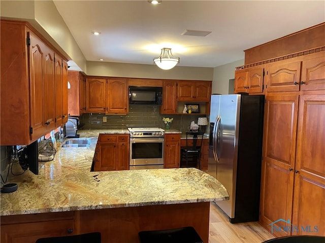 kitchen featuring a peninsula, tasteful backsplash, appliances with stainless steel finishes, and light stone counters