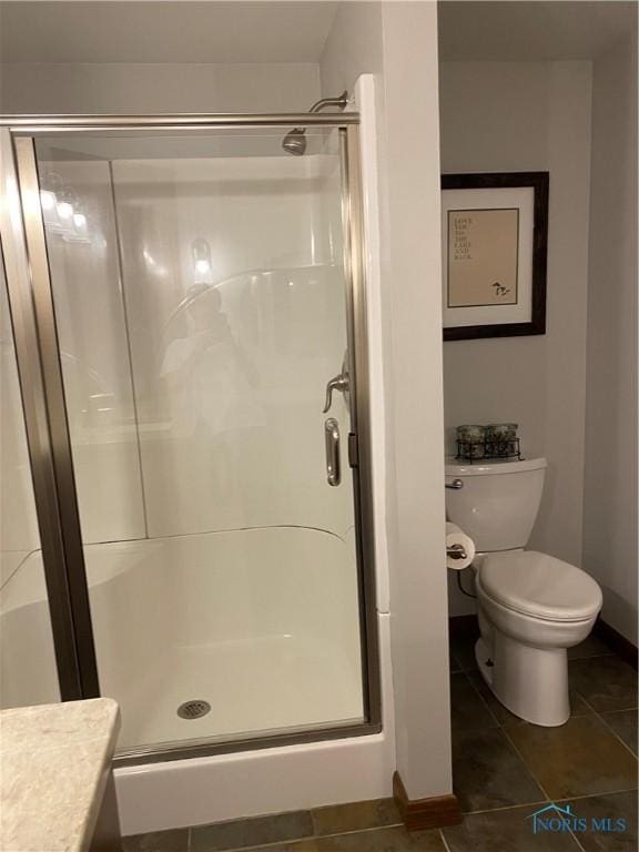 bathroom with tile patterned floors, toilet, a stall shower, baseboards, and vanity
