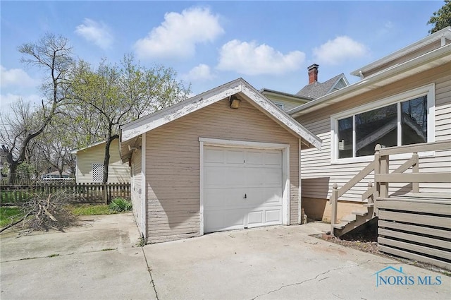 detached garage featuring concrete driveway and fence