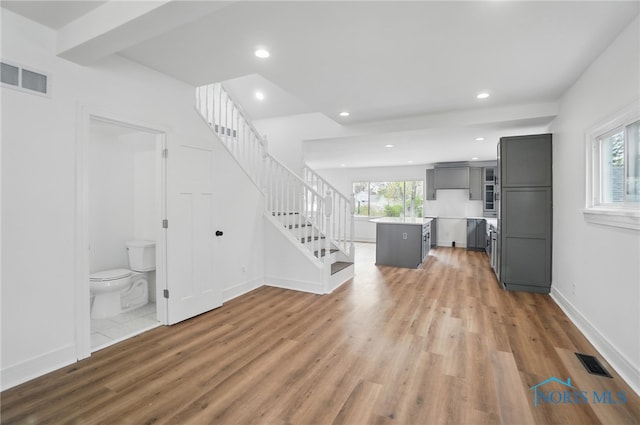 unfurnished living room featuring stairway, wood finished floors, and visible vents