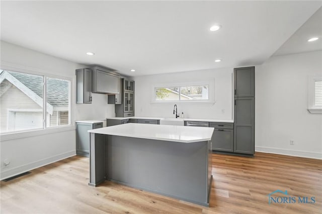 kitchen featuring a center island, light wood-style flooring, a sink, recessed lighting, and gray cabinets