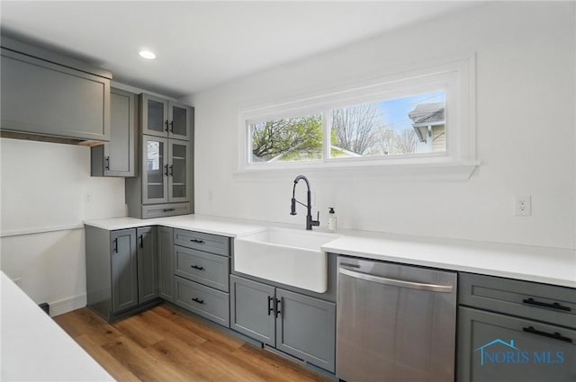 kitchen with wood finished floors, dishwasher, gray cabinetry, and a sink