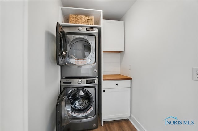 clothes washing area featuring baseboards, cabinet space, stacked washing maching and dryer, and dark wood-style floors